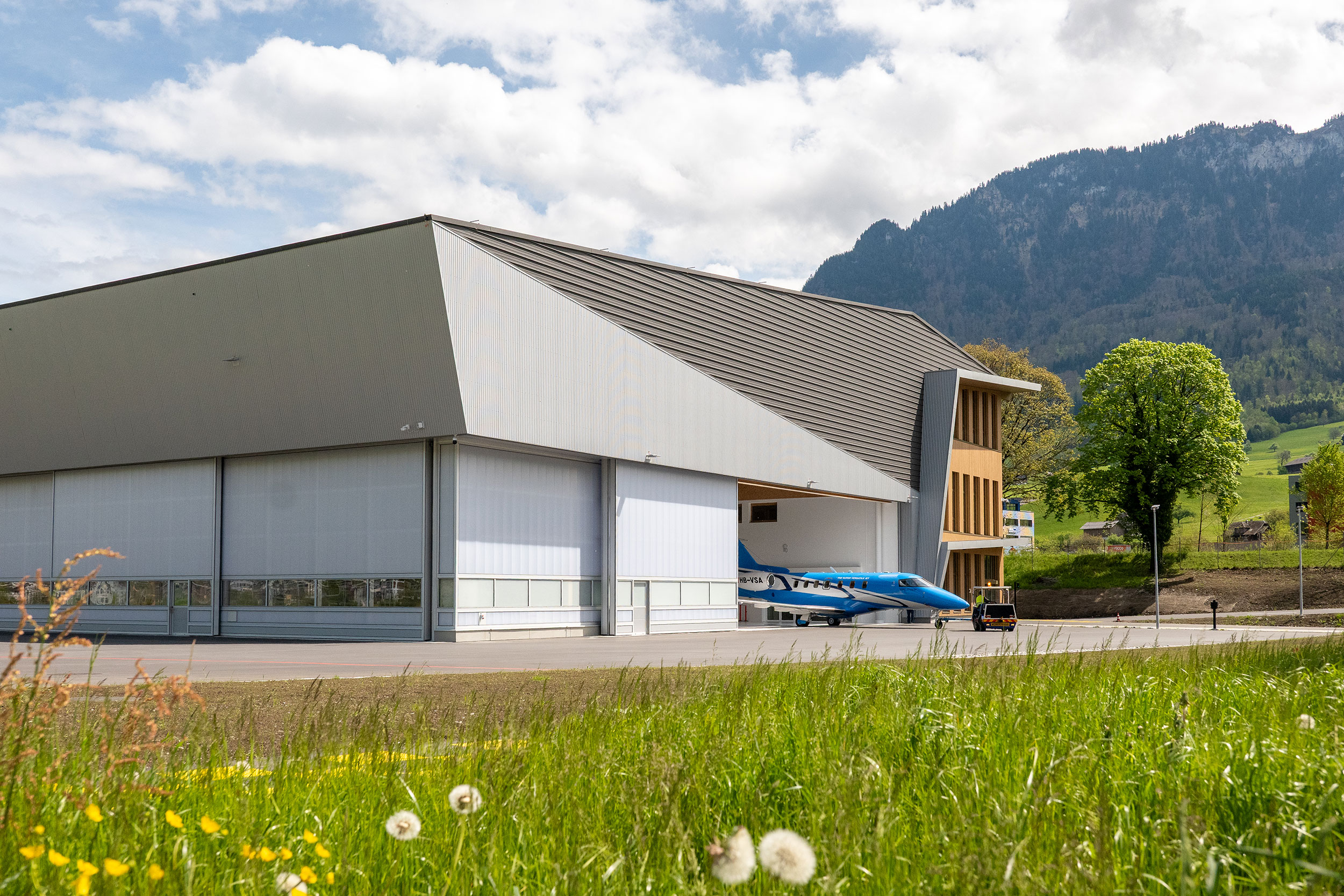 Wartungshalle Brisen in Buochs mit geöffnetem Hangartor, Flugzeug auf dem Vorfeld und Bergkulisse