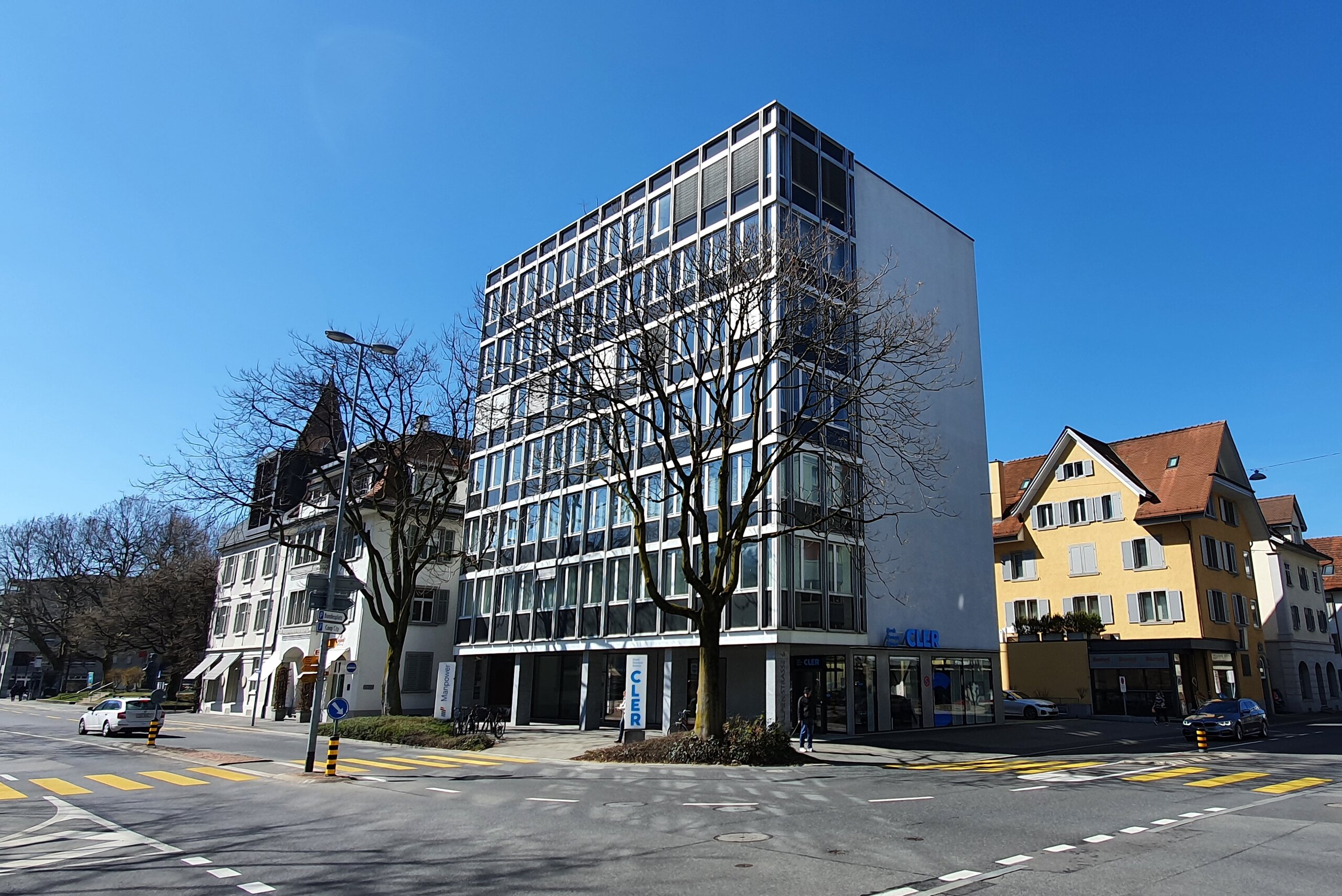 Saniertes Geschäftsgebäude mit Fensterbändern zwischen zwei Altbauten an einer Kreuzung