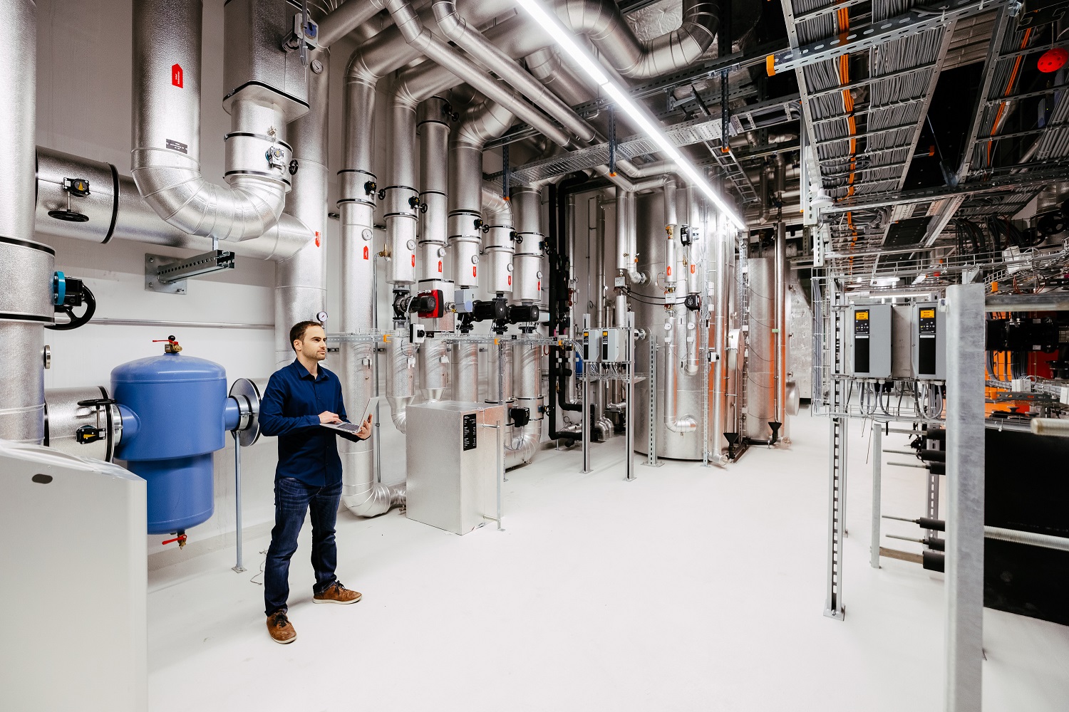 Ingenieur mit Laptop in der Energiezentrale zwischen Verteilern und Wärmetauschern