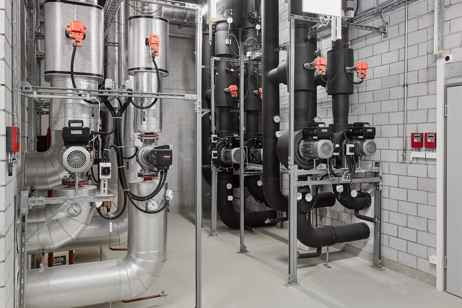 Pumpen mit Motoren und Armaturen an gedämmten Rohrleitungen in einer Technikzentrale