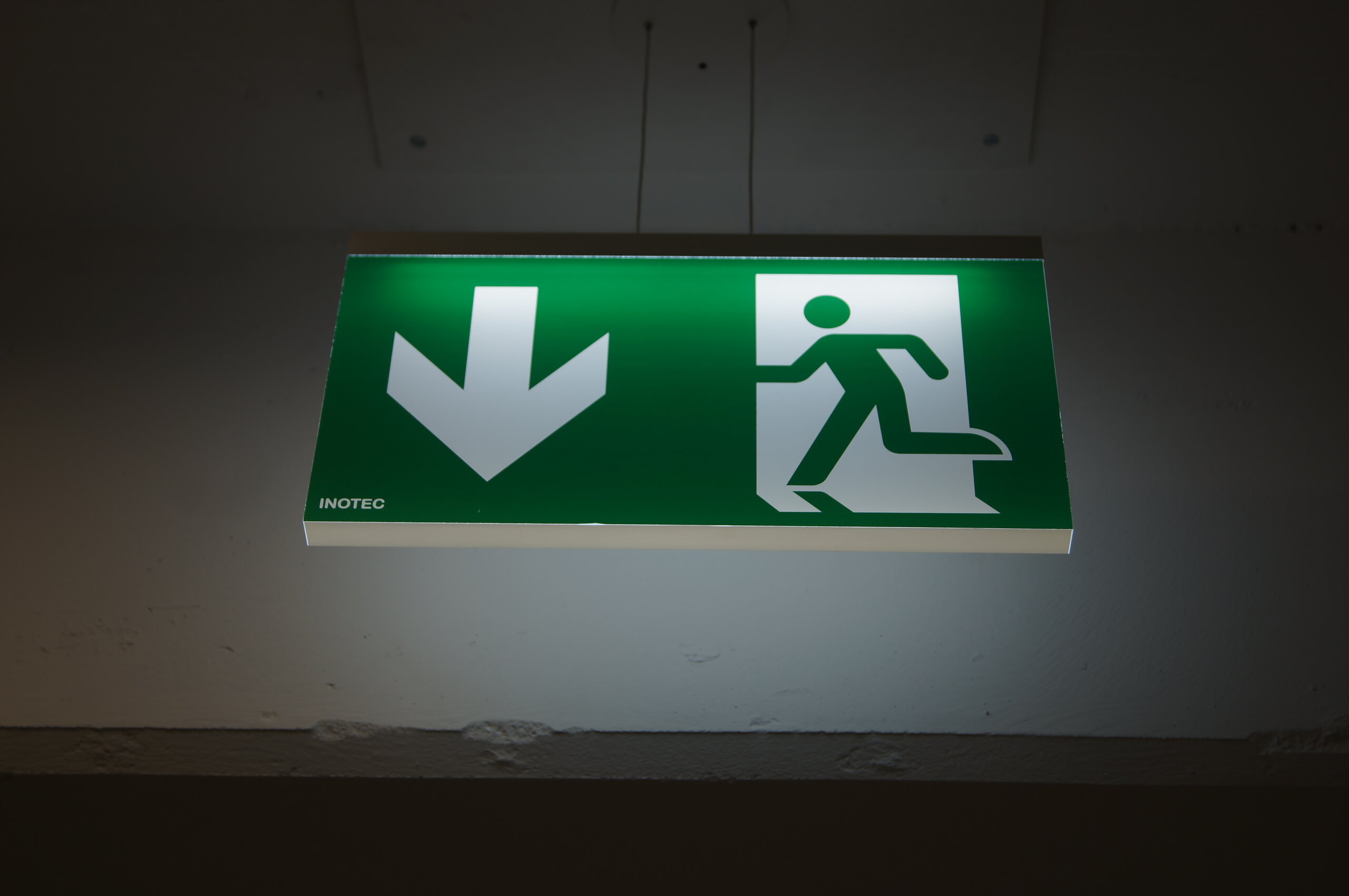 Beleuchtetes grünes Fluchtwegschild mit Pfeil und Notausgangssymbol