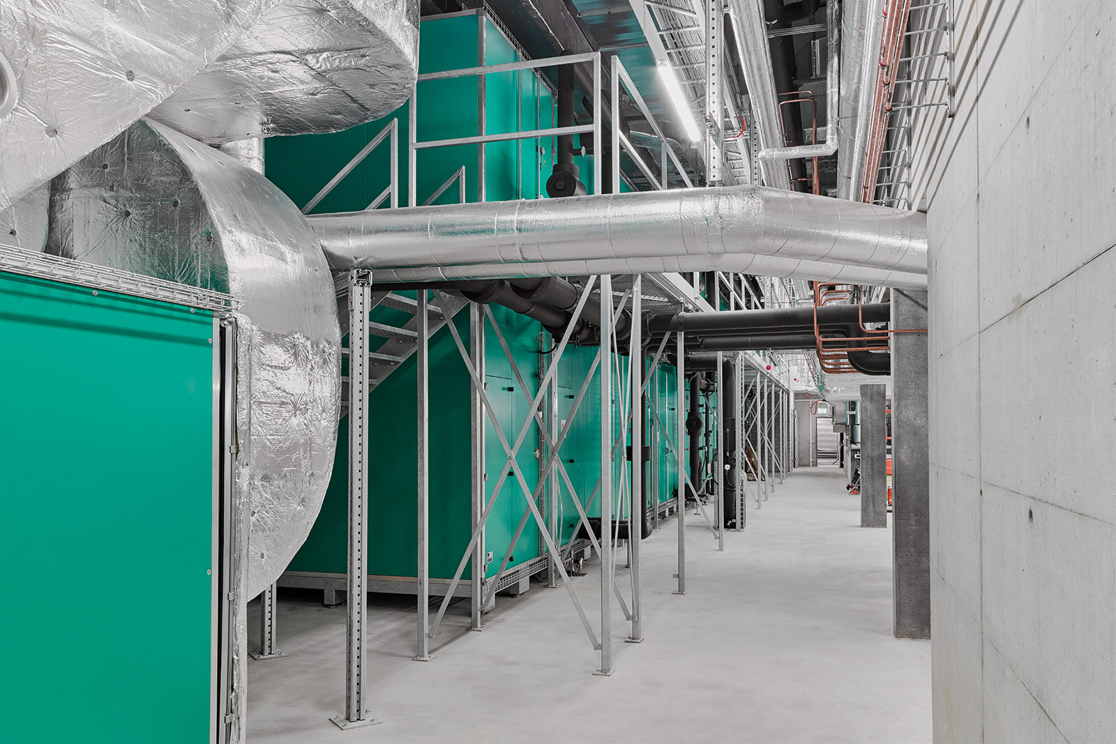 Grüne Lüftungsmonoblocks und gedämmte Kanäle in einem Technikgeschoss mit Betonwand
