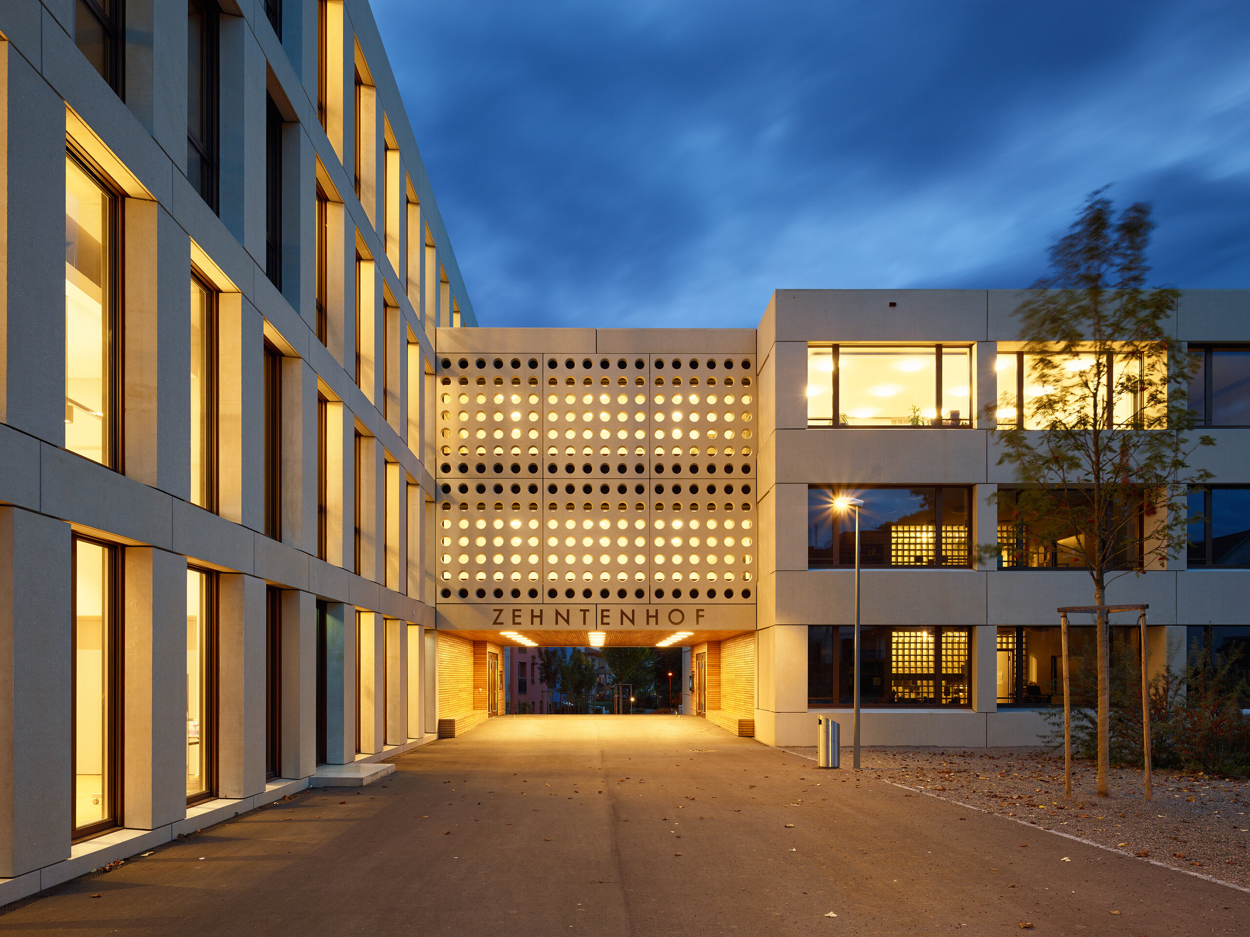 Schulhaus Zehntenhof in der Abenddämmerung mit beleuchtetem Durchgang und Schriftzug